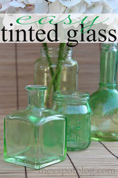 three green glass vases sitting on top of a wooden table next to white flowers