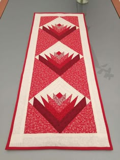 a red and white quilted table runner on top of a gray surface with flowers