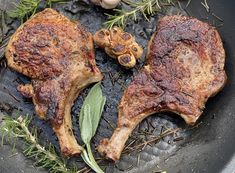 two pieces of meat sitting on top of a pan with herbs and spices next to it