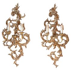 a pair of wall sconces with candles in the middle and an intricately carved design