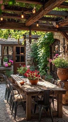 an outdoor dining area with potted plants and hanging lights above the table, surrounded by stone walls