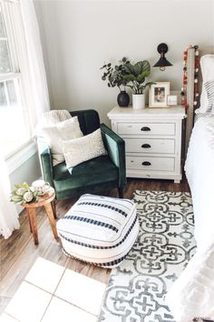 a bedroom with a green chair, white bed and rugs on the wooden floor