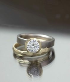 two wedding bands with a diamond in the middle and one on top, sitting next to each other