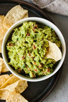 a bowl of guacamole and tortilla chips on a black plate