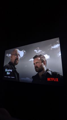 two men are on a television screen in the dark, one is staring at another man