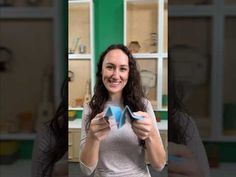 a woman holding up two pieces of paper in front of her face and smiling at the camera