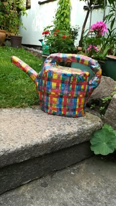 a colorful watering can sitting on top of a stone step in front of some flowers