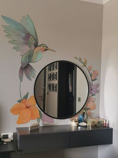 a mirror sitting on top of a dresser next to a wall with flowers painted on it