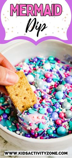 a hand dipping a cracker into a bowl filled with colorful sprinkles