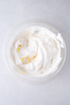 a bowl filled with whipped cream on top of a white countertop next to a spoon