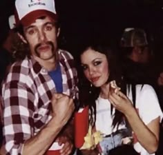 a man and woman posing for the camera with some food in their hands at a party