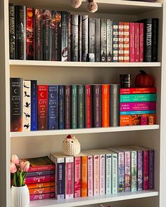 a book shelf filled with lots of books next to a white vase full of flowers