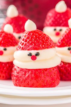 some red strawberries with white frosting and santa hats on them, sitting next to other small ones