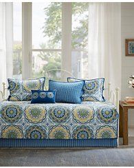 a day bed with blue and yellow pillows in front of a large window that has white curtains