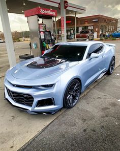 a silver chevrolet camaro is parked in front of a gas station