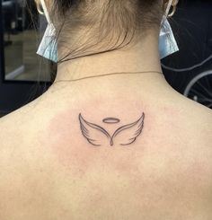 the back of a woman's neck with an angel wing tattoo on her left shoulder