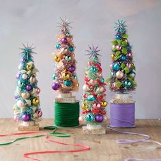 three small christmas trees made out of yarn on a table next to twine spools