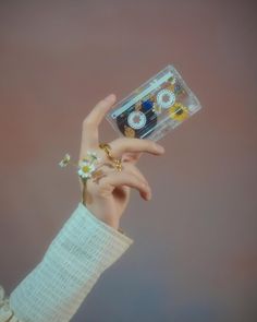 a person holding up a plastic container with jewelry in it's palm, against a pink background