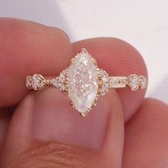 a close up of a person's hand holding a ring with an oval shaped diamond