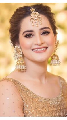 a woman in a gold dress with pearls on her head and large earrings, smiling at the camera