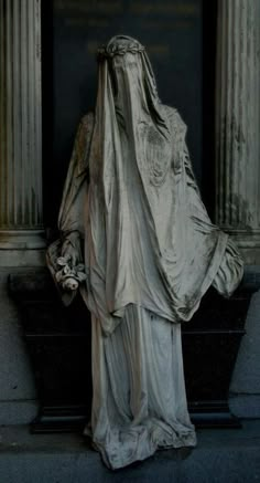 the statue is wearing a veil and standing in front of an old building with columns