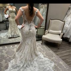 a woman standing in front of a mirror wearing a wedding dress with an open back