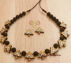 a necklace and earring set with black beads on a wooden surface, decorated with gold accents