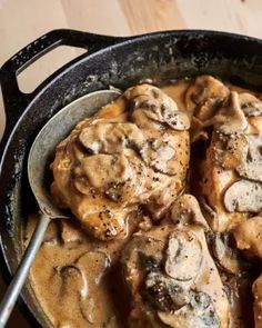 a skillet filled with meat covered in mushroom gravy on top of a wooden table