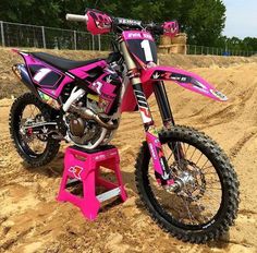 a pink dirt bike parked on top of a dirt field