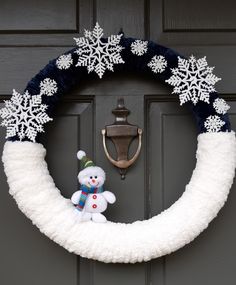 a wreath with snowflakes and a teddy bear is hanging on the front door