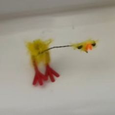 two small yellow and red birds on a white surface with one holding the other's tail