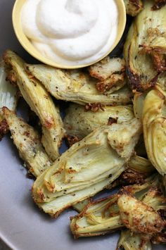 grilled artichokes with sour cream on the side in a white bowl