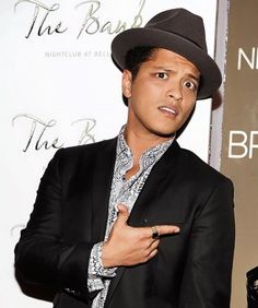 a man in a black suit and hat pointing to the side with his hand on his hip