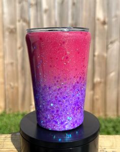 a purple and pink cup sitting on top of a black stand in front of a fence