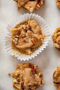 several cupcakes with nuts and other toppings in paper cups on a white surface