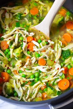 a pot filled with chicken, carrots and peas next to a wooden ladle