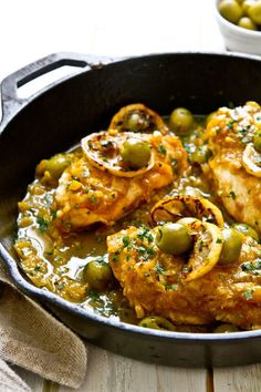 a pan filled with chicken and olives on top of a wooden table