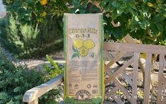 a bag sitting on top of a wooden bench next to a green bush and tree