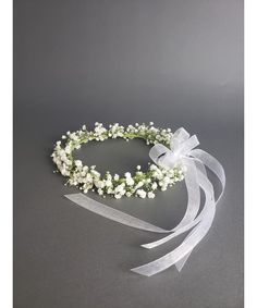 a flower crown with white flowers and ribbon tied around the headband on a gray background