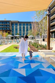 a woman in white dress walking on blue and white tiled floor next to a building