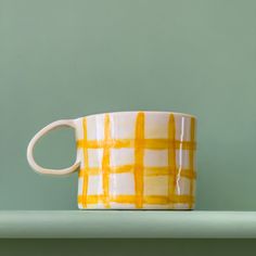 a yellow and white coffee cup sitting on top of a shelf next to a green wall