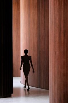 a woman in a black dress is walking through an empty room with wooden walls and columns