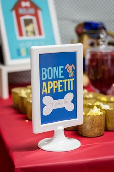 Party display with a blue sign in white frame that reads "Bone Appetit, It's Chow Time". Has a cartoon puppy on it for a puppy birthday party. Puppy Birthday Theme, Puppy Invitations, Coco Birthday, Adopt A Puppy, Emily English