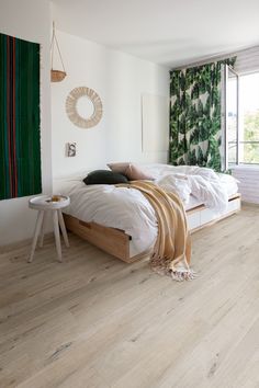 a bedroom with wood flooring and white walls is pictured in this image, there are pillows on the bed