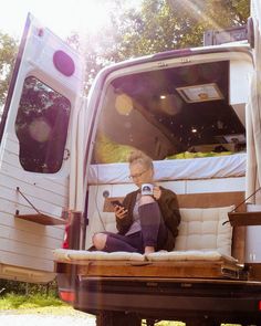 a man sitting in the back of a truck looking at his cell phone while holding a camera