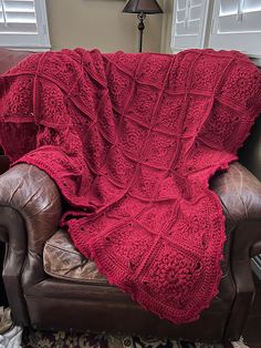 a red crocheted blanket is draped over a brown leather chair in a living room