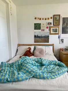 an unmade bed in a bedroom with pictures on the wall above it and a teddy bear