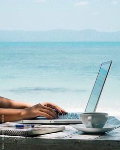 a woman sitting at a table with a laptop computer on her lap by the ocean