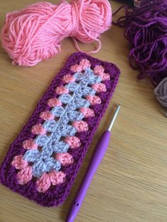 a crochet granny next to some yarn and a ball of knitting needles on a table