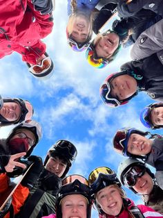 a group of skiers standing in a circle looking up at the camera and smiling